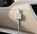 A single premium square-shaped white alloy magnetic cable clip mounted flush on a stitched cream leather car dashboard, holding a white charging cable cleanly in place under crisp, natural daylight.